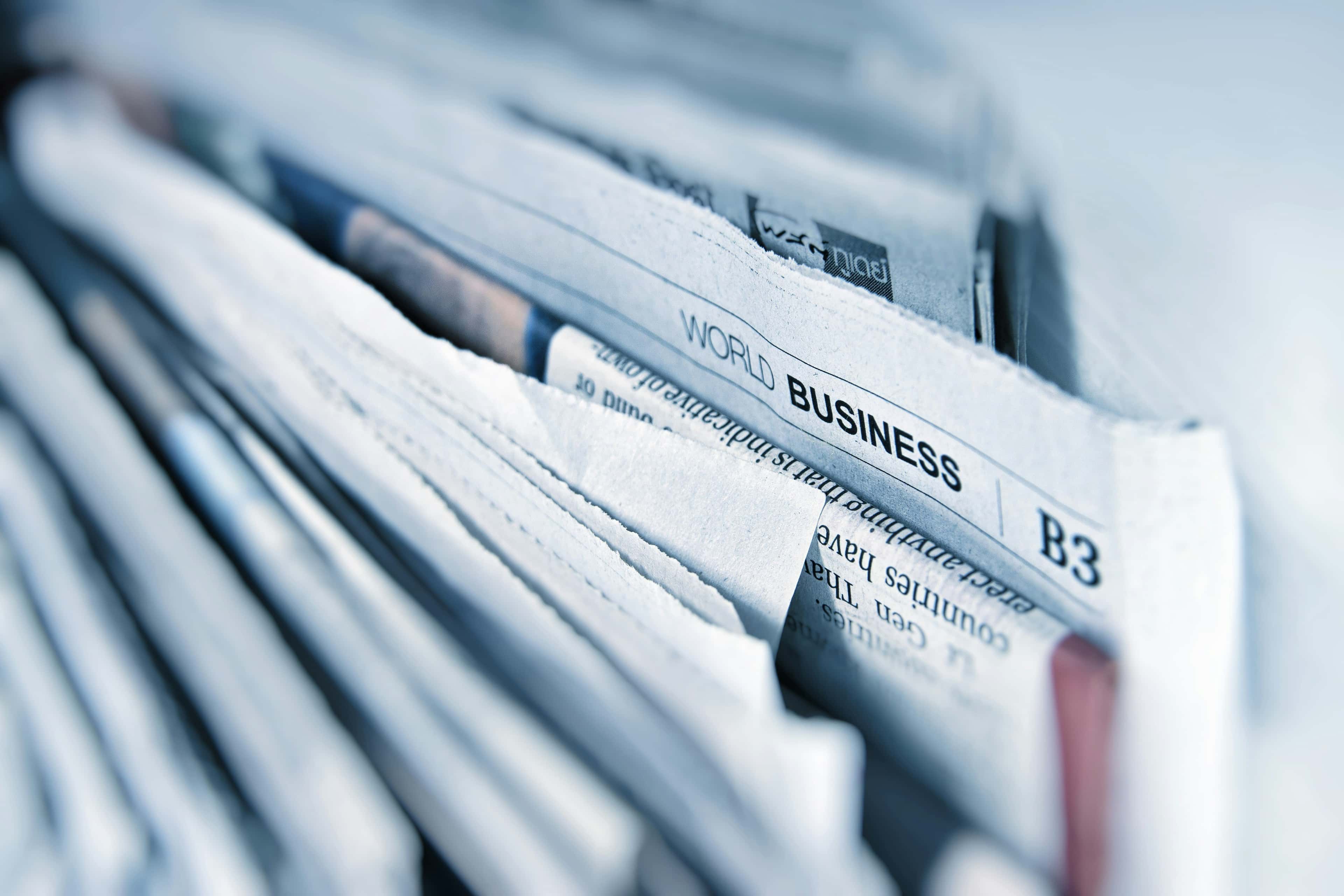 Stack of folded newspapers with "Business" section visible on top, shown in shallow depth of field