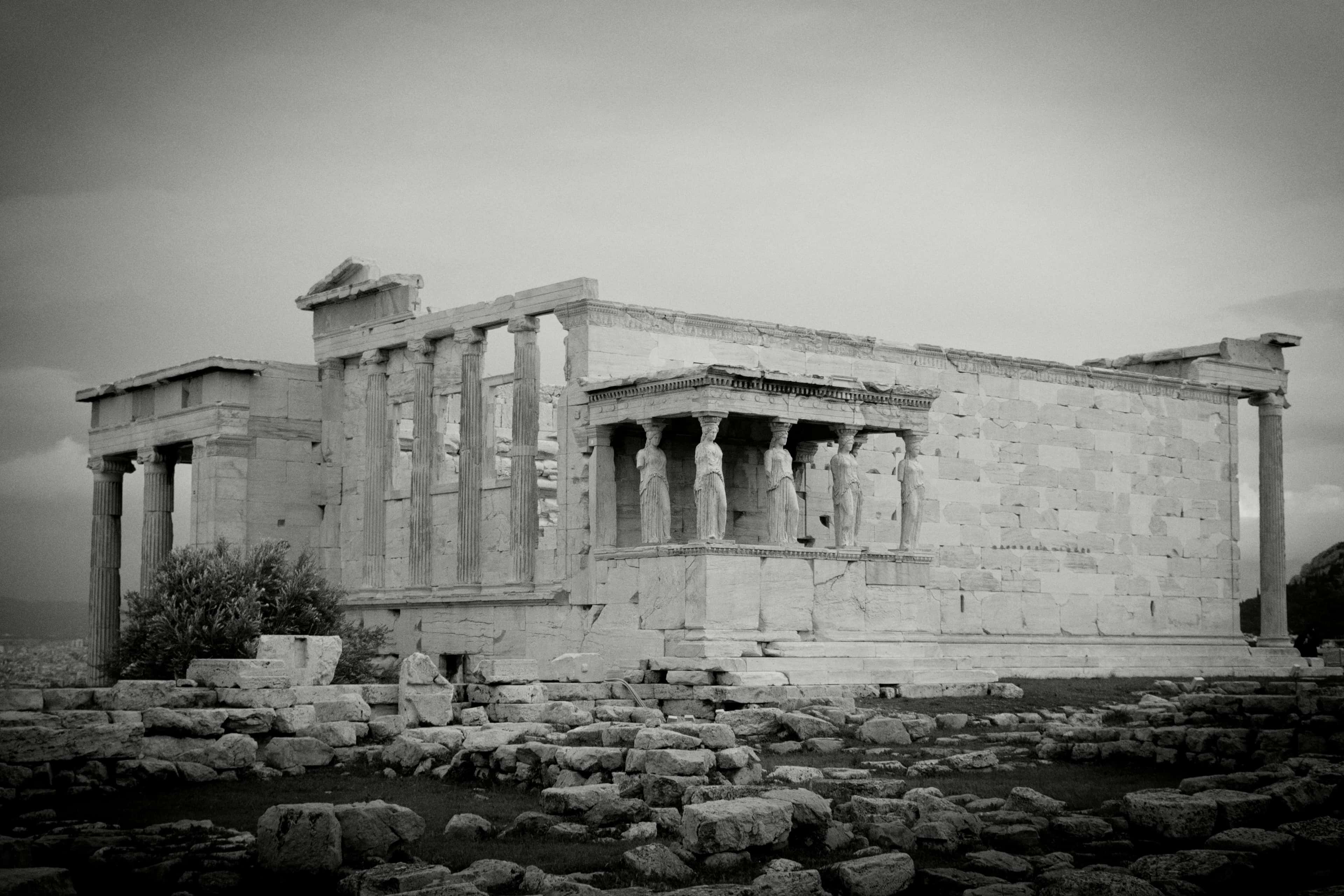Ancient Greek temple with columns and partially ruined walls on rocky ground, black and white photograph